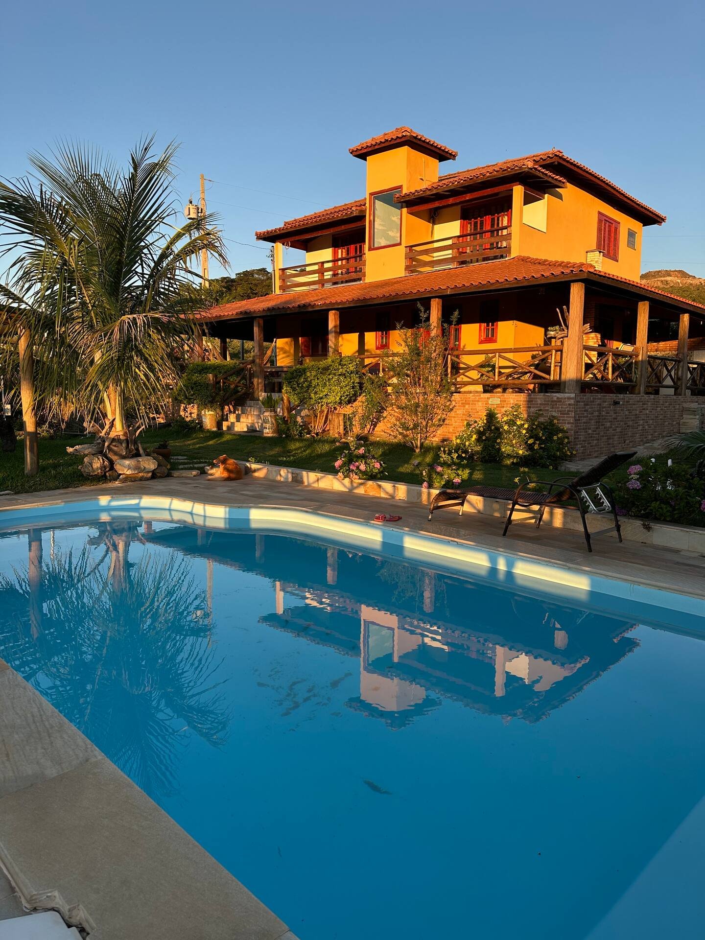Casa grande e piscina iluminadas pela luz do fim da tarde.