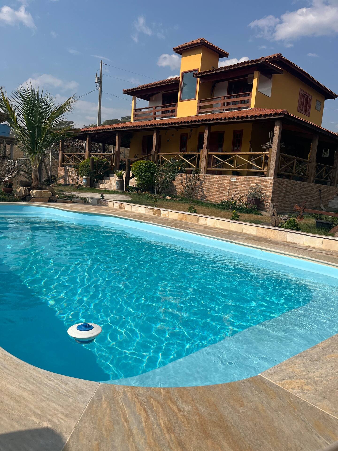Piscina azul em primeiro plano e casa grande ao fundo, durante o dia.