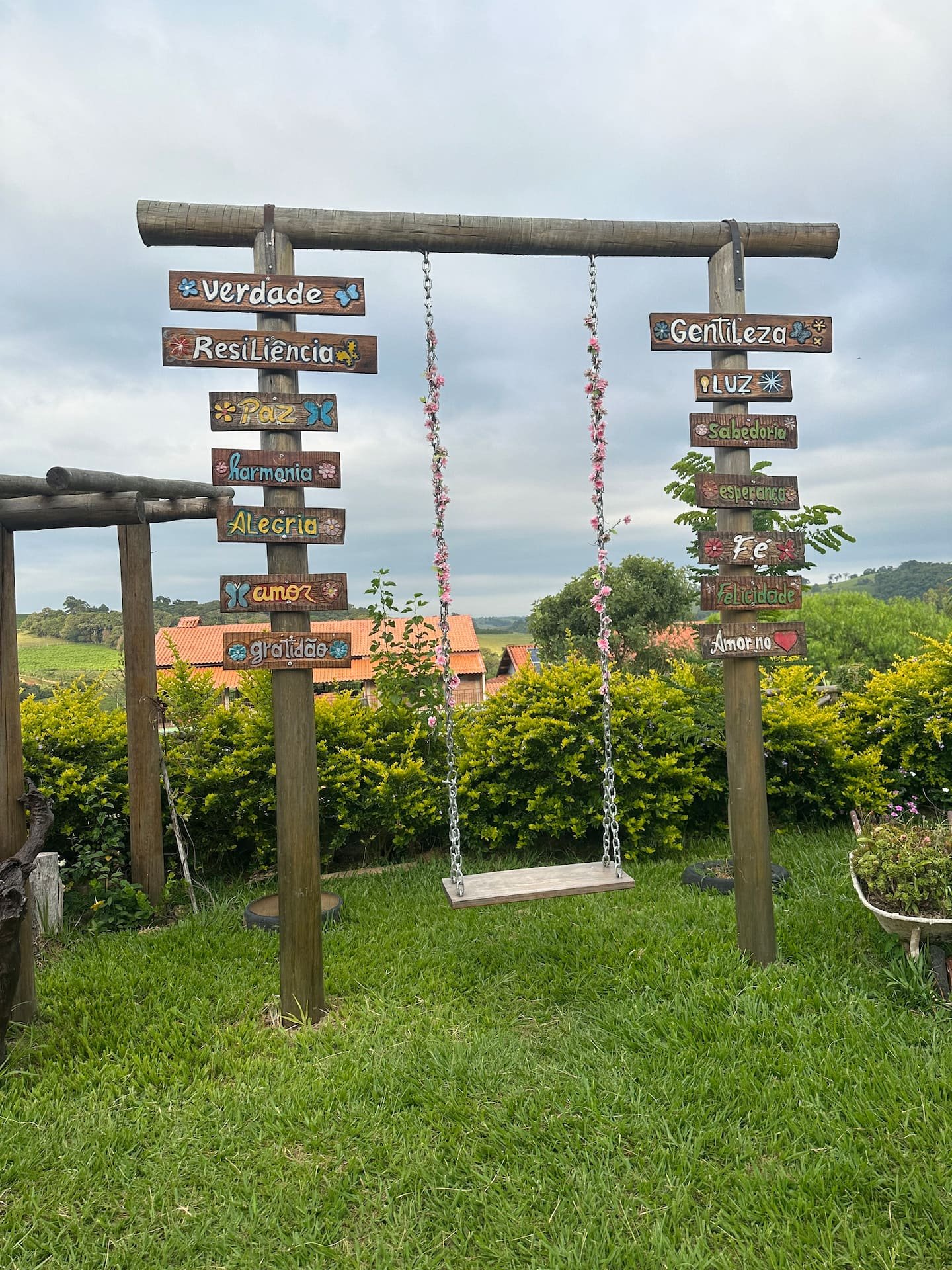Balanço de madeira e gramado do jardim, com placas decorativas e vegetação.