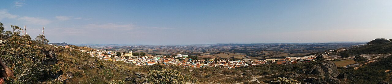 Vista panorâmica real de São Thomé das Letras, com cidade, rochas e horizonte de montanhas.